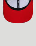 Close-up of the red curved brim with black trim on a white Haas cap.