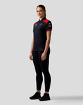 Model wearing Haas Team Women's Short Sleeve Polo in navy with red shoulder panels and front sponsor logos.