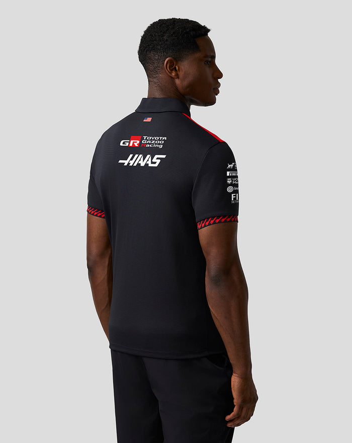 Back view of a man in a black Haas Team polo displaying large Haas branding and sponsor logos on the upper back.