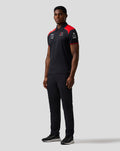 Side view of a man in a black Haas Team polo with red shoulder accents and sponsor logos on the sleeve.