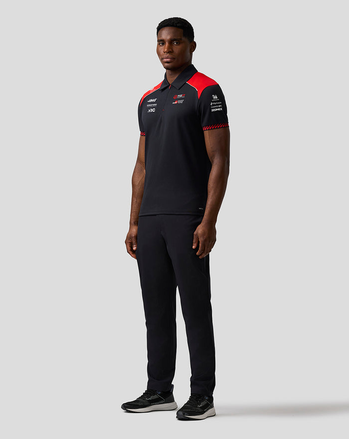 Side view of a man in a black Haas Team polo with red shoulder accents and sponsor logos on the sleeve.