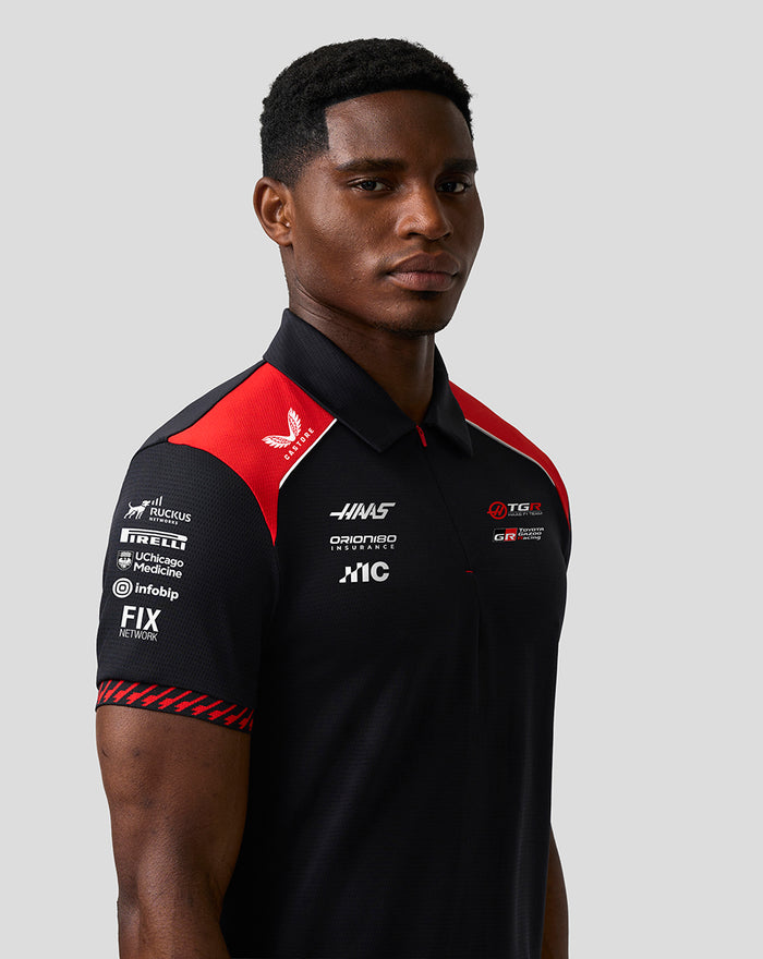 Model wears Official Haas Team Short Sleeve Polo in black with red shoulder panels and front sponsor logos.