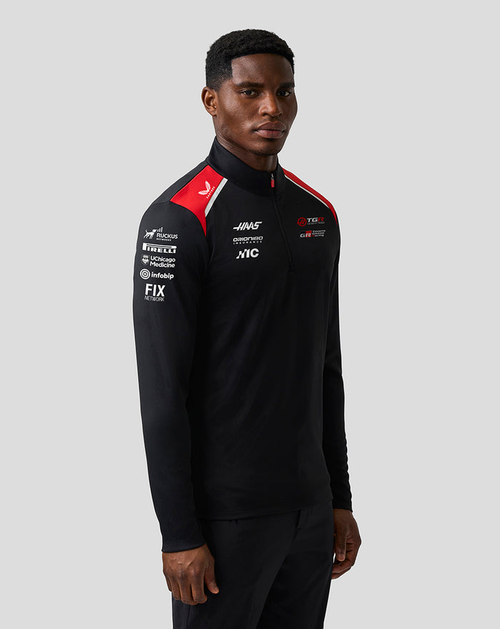 Male model wearing Haas Team Quarter Zip Midlayer in black with red shoulder panels and sponsor logos on the chest