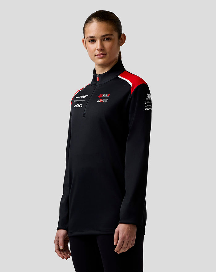 Female model wearing Haas Team Quarter Zip Midlayer in black with red shoulder panels and logo details on the chest and sleeve