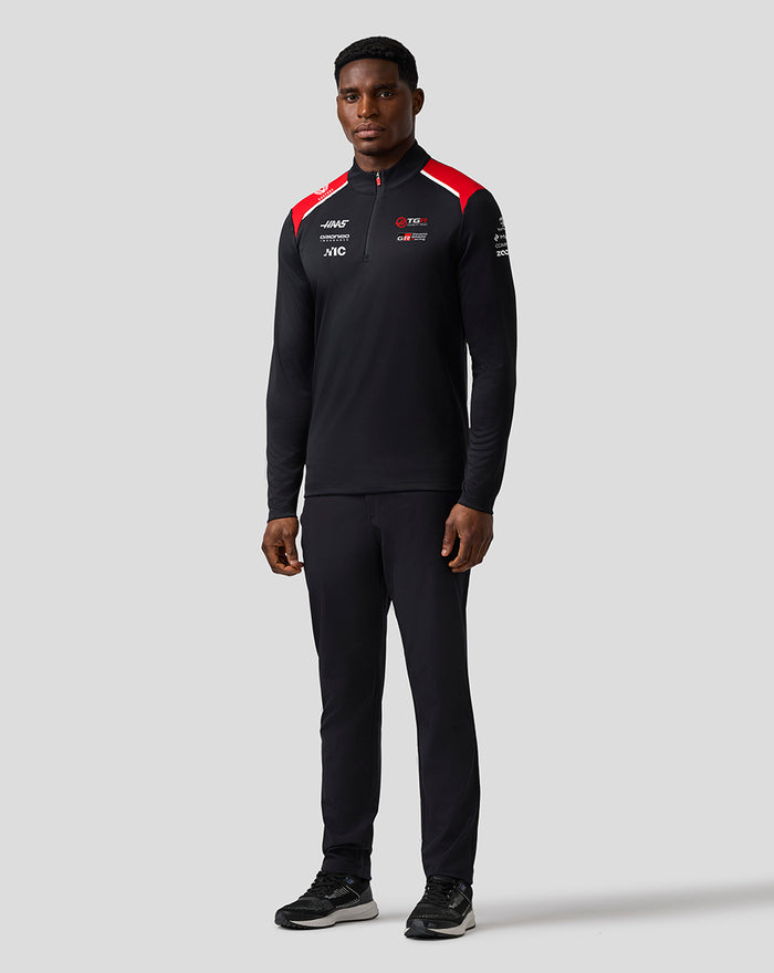 Front view of a man wearing the Haas Team Quarter Zip Midlayer with red shoulder panels and sponsor logos on the chest and sleeve.