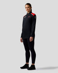 Female model wearing Haas Team Quarter Zip Midlayer in black with red shoulder panels and sponsor logos on the chest.