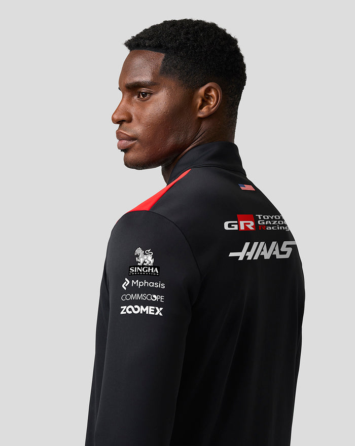 Rear three quarter view of a model in the Haas Team Quarter Zip Midlayer, showing large Haas and sponsor logos on the back.