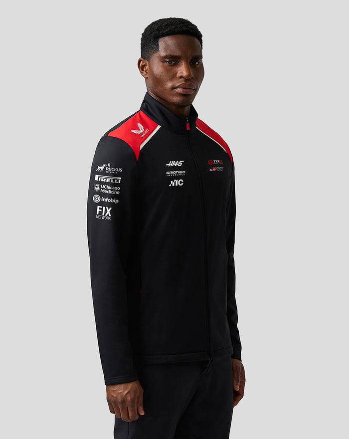 Male model wearing Haas Team Soft Shell Jacket with red shoulder panels and prominent branding on the chest in a studio shot