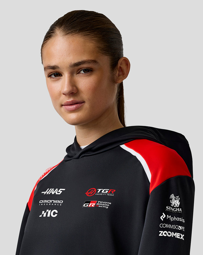 Model wearing the Official Haas Team Pullover Hoodie with black base and red shoulder panels showcasing chest logos.