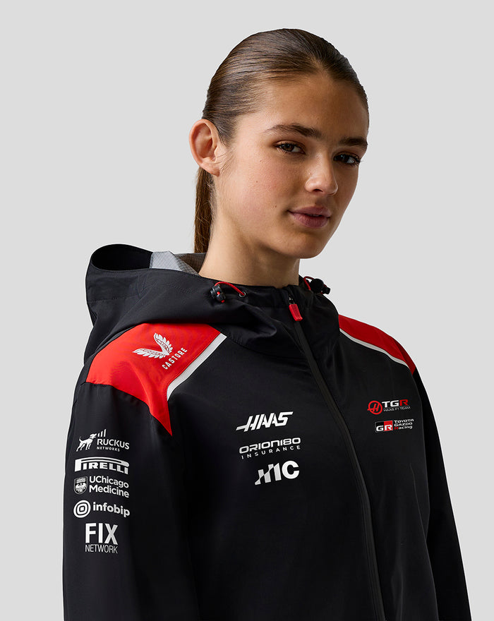 Female model wearing Haas Team water resistant jacket featuring red accents and sponsor logos on the chest and sleeve.