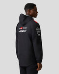 Back view of Haas Team water resistant jacket on a male model, hood visible, red shoulder panels and sponsor logos on the sleeve.