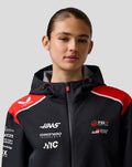 Female model wearing a Haas Team water resistant jacket with hood and red accents; Castore badge and sponsor logos visible
