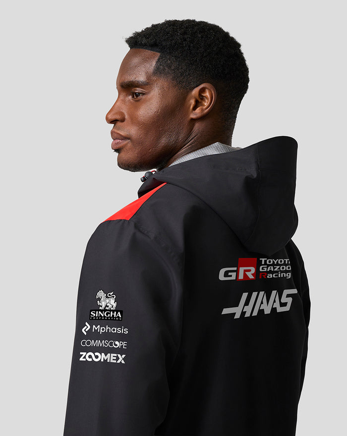 Male model wearing Haas Team water resistant jacket shown in profile with hood and large back branding logos.