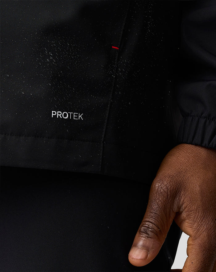 Close up of Haas Team water resistant jacket showing ProTEK logo on black fabric and a glimpse of the elastic cuff