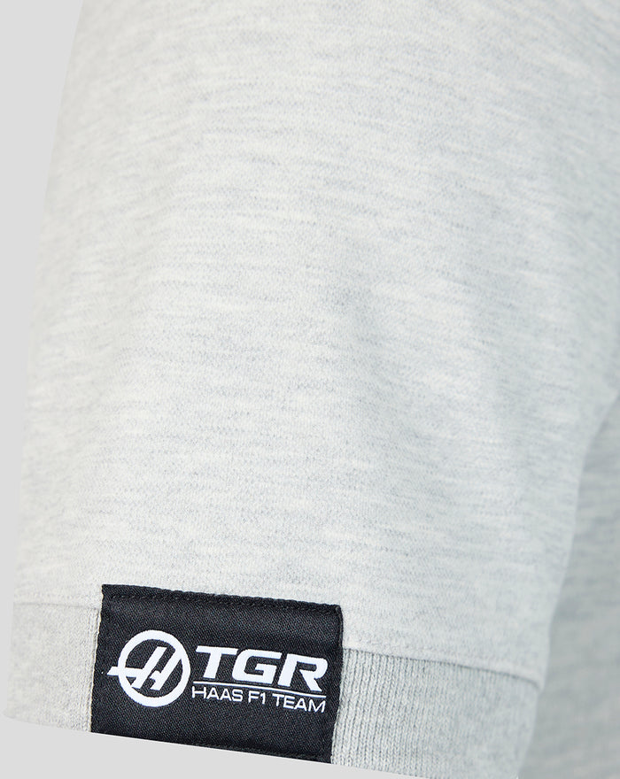 Close-up of sleeve hem with black TGR Haas F1 Team woven label on light gray polo.