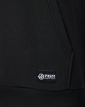 Close-up of black Haas hoodie fabric with a woven sponsor label at the lower left front hem.