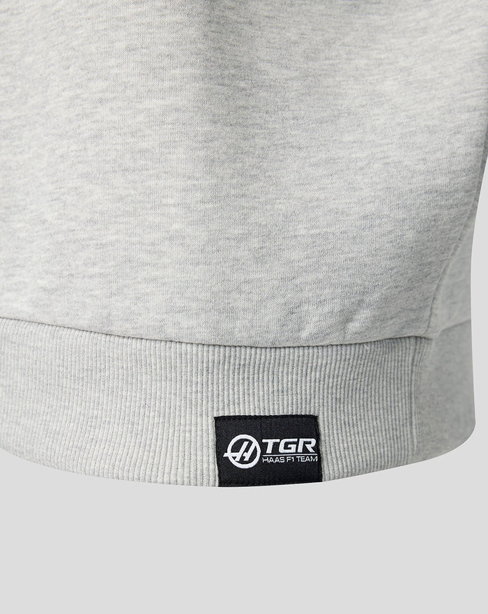 Close up of the grey heather Haas quarter zip hem with black woven TGR Haas F1 Team label at the lower left front.