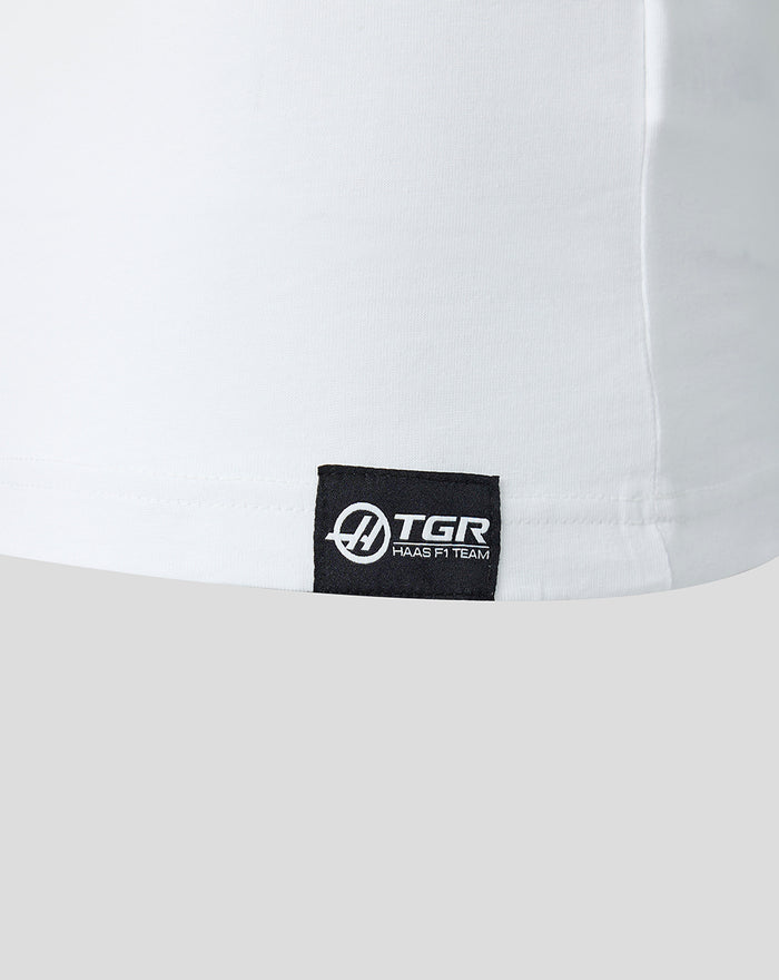 Black woven label with sponsor branding at the lower left front hem on a white T shirt